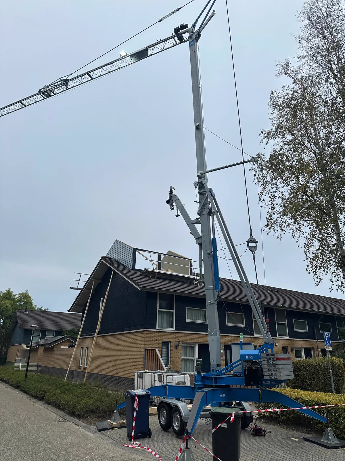 Hijskraan opgesteld voor de woning tijdens het plaatsen van de nokverhoging